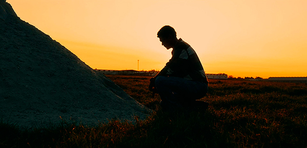 Silhueta de agricultor ajoelhado ao lado de monte de terra ao pôr do sol